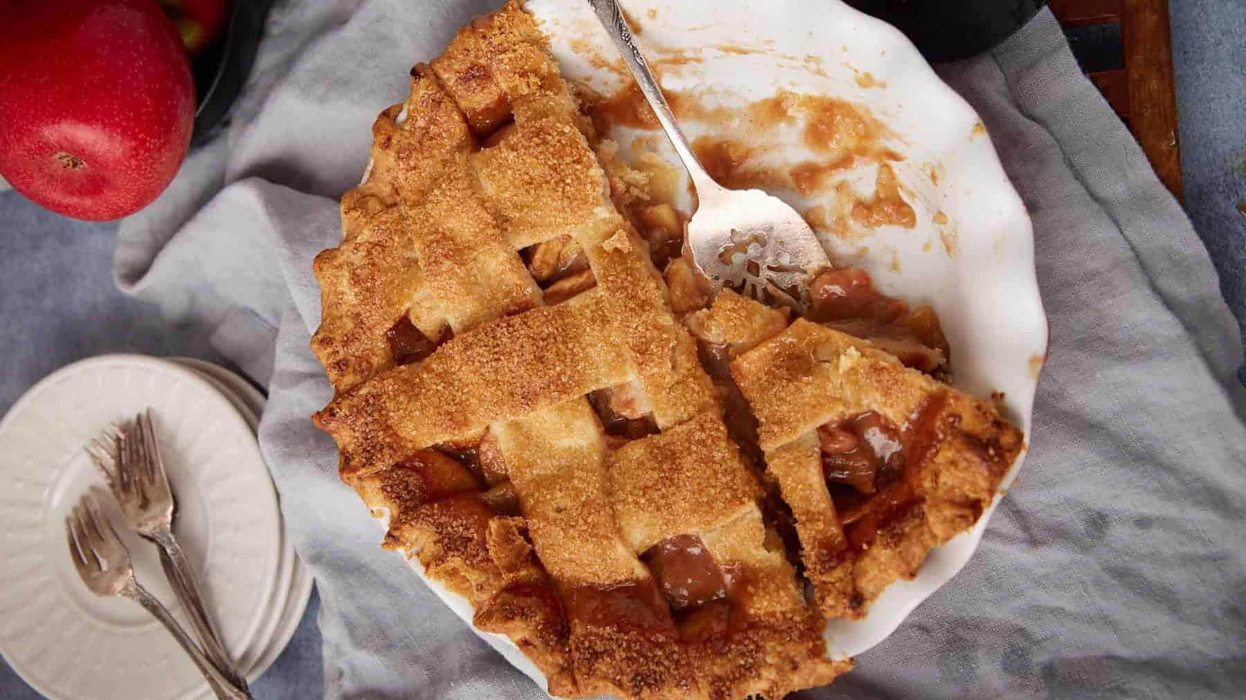 caramel apple pie in a white pie dish with two pieces taken out of it.