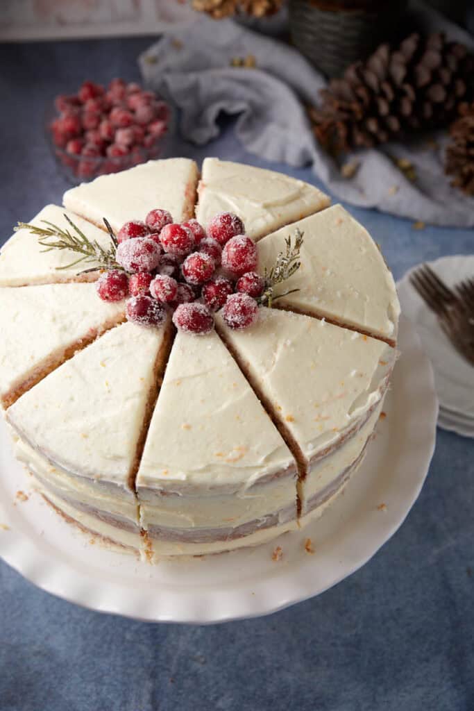 Top-down view of a sliced cranberry layer cake, decorated with sugared cranberries and rosemary, ready to serve.