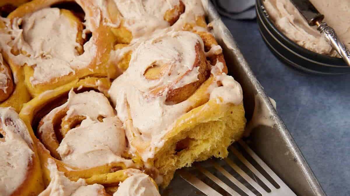 iced pumpkin cinnamon rolls in a baking dish with a spatula.
