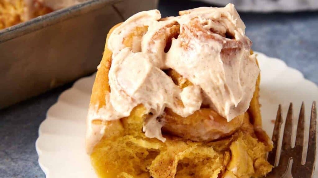 iced pumpkin cinnamon roll on a white plate with a fork.