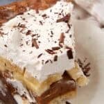 A plated slice of Banoffee Pie with a fork beside it, showing caramel and banana layers under whipped cream.