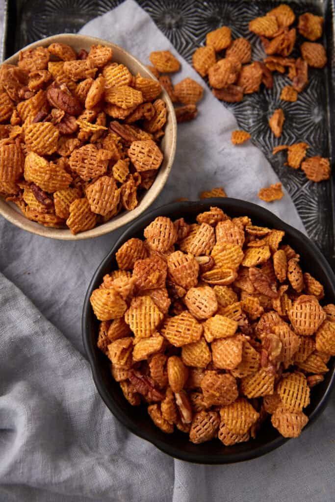 Two bowls filled with golden, crunchy caramel cereal mix on a tray lined with a gray linen napkin.