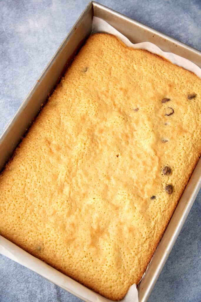 Baked white chocolate blondie slab in a metal pan, cooling on parchment paper before frosting.