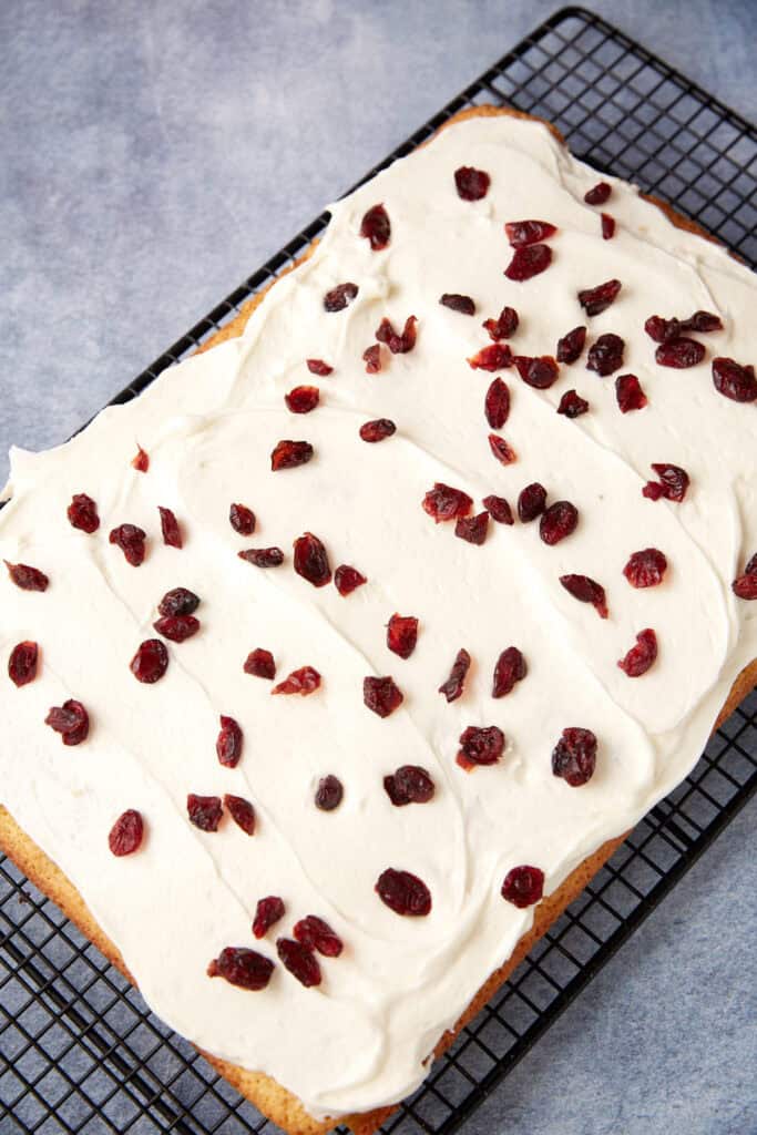 Cranberry Bliss Bars decorated with cranberries on a wire rack.