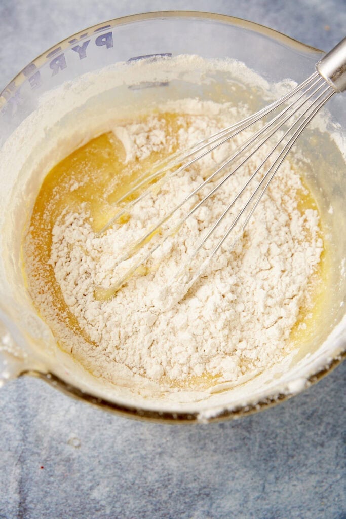 Dry ingredients, including flour and leavening, added to the wet batter in a mixing bowl.