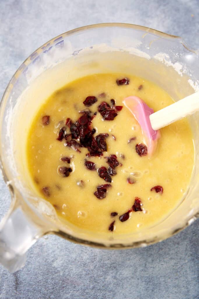 Dried cranberries being folded into the blondie batter with a pink spatula.
