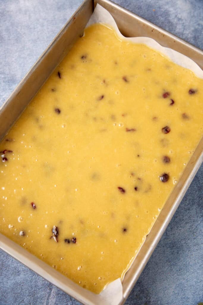 Cranberry blondie batter spread evenly in a parchment-lined baking pan before baking.