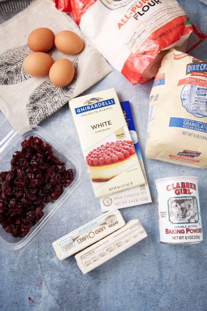 Flat lay of baking ingredients including white chocolate, dried cranberries, butter, sugar, flour, and eggs for Cranberry Bliss Bars.