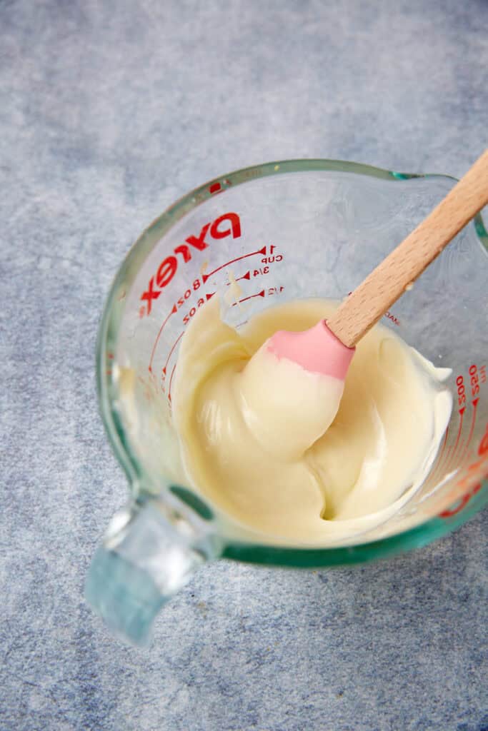 Melted white chocolate stirred in a glass measuring cup, ready to be added to the cream cheese frosting.