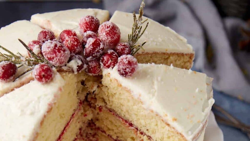 The whole cranberry cake on a stand with several slices removed, showing the inside layers and cranberry filling.