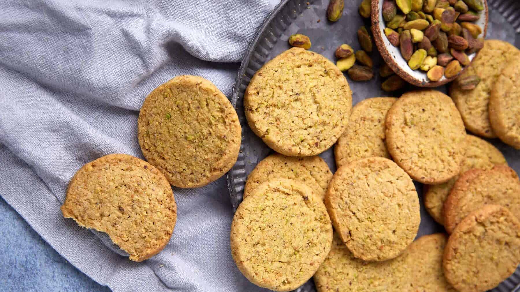 A tray filled with golden pistachio shortbread cookies and a small bowl of pistachios.