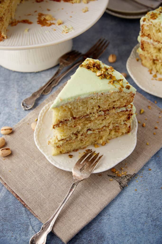 Slice of Watergate Cake on a white plate, showing pale green frosting and three pistachio-studded layers.