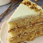 Slice of Watergate Cake on a white plate, showing pale green frosting and three pistachio-studded layers.