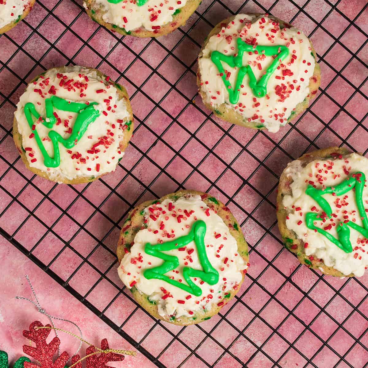 Decorated Christmas sprinkle cookies cooling on a wire rack with green icing trees and red sprinkles.