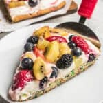 Slice of fruit pizza on a white plate topped with strawberries, kiwi, blueberries, and blackberries over cream cheese frosting.