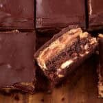 Peanut butter brownies cut into rows on a wooden board, with one square lifted to display the dense brownie and peanut butter layers.