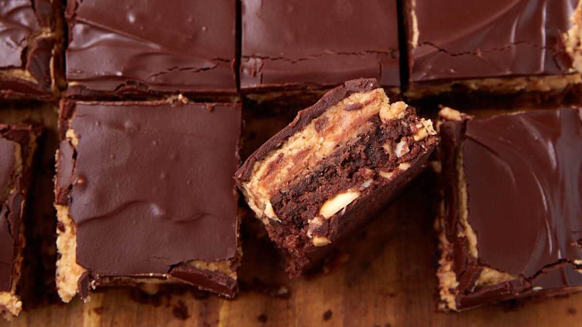 Peanut butter brownies cut into rows on a wooden board, with one square lifted to display the dense brownie and peanut butter layers.