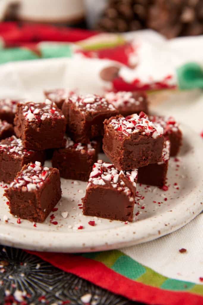 Small squares of chocolate peppermint fudge arranged on a speckled plate, topped with crushed peppermint candy.