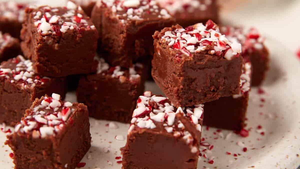 Small squares of chocolate peppermint fudge arranged on a speckled plate, topped with crushed peppermint candy.