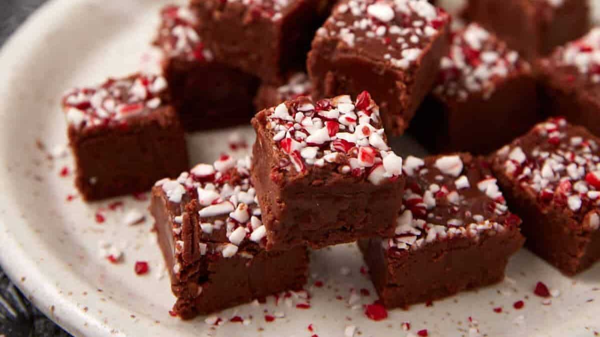 Small squares of chocolate peppermint fudge arranged on a speckled plate, topped with crushed peppermint candy.