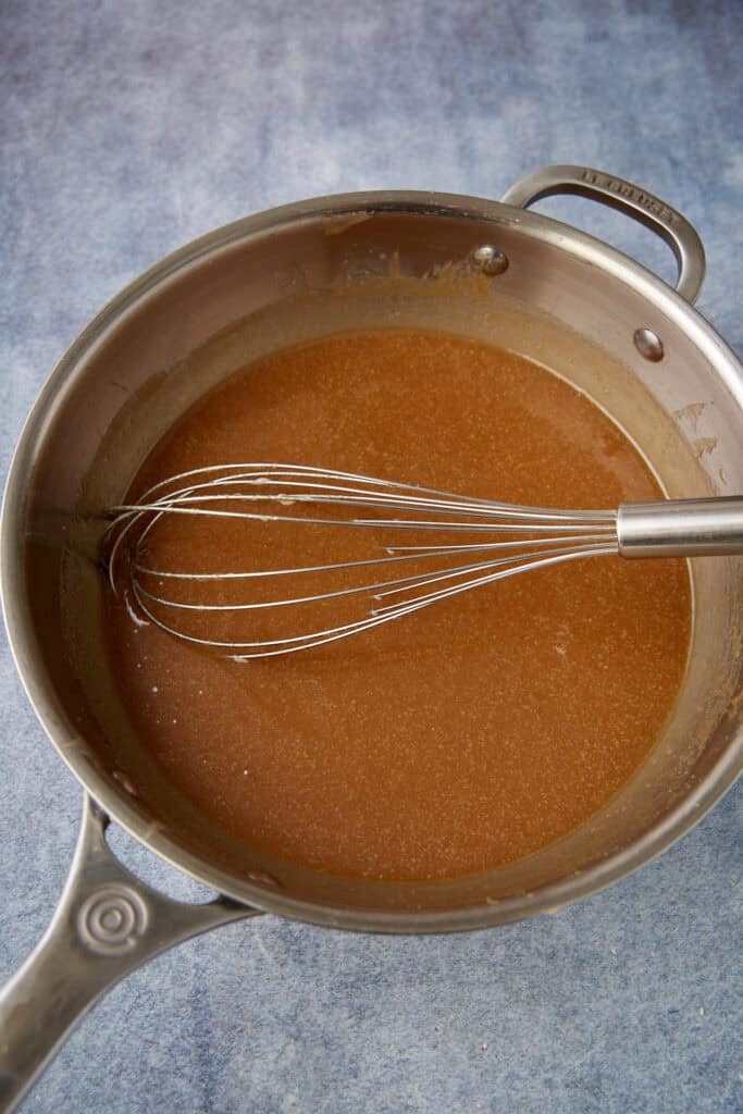 Melted sugar, butter, and milk mixture in a saucepan being whisked into a smooth base for fudge.