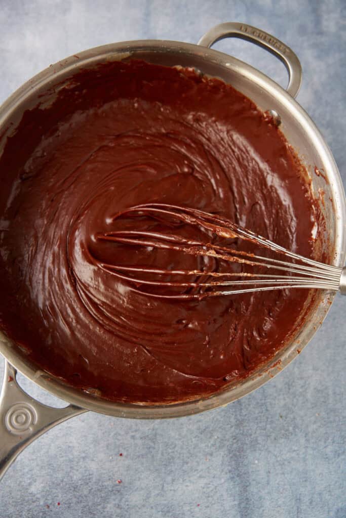 Chocolate and marshmallows melted into a thick, smooth fudge mixture being whisked in a saucepan.