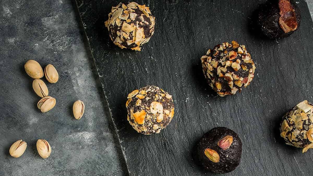 Assorted chocolate truffles with nut, cocoa powder, and sugar coatings arranged on a slate board.