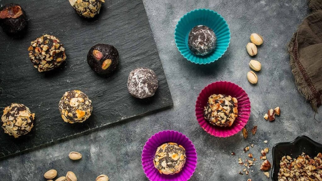 Assorted chocolate truffles with nut, cocoa powder, and sugar coatings arranged on a slate board.