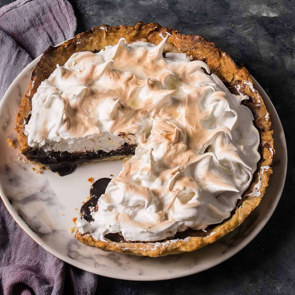 Close-up overhead shot of a chocolate meringue pie with a large slice removed.
