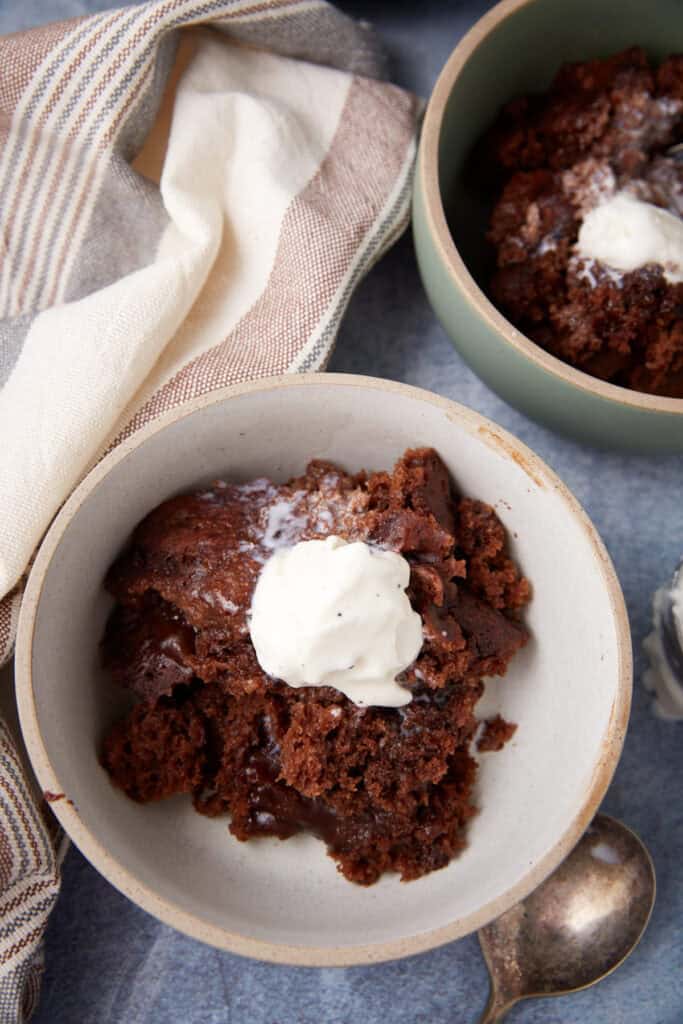 Two bowls of chocolate lava cake topped with ice cream on a blue surface, with a striped kitchen towel and a spoon nearby.