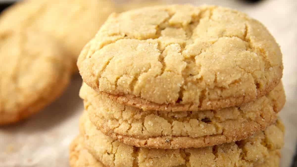 Tall stack of lemon cornmeal rosemary cookies on a cloth, showing their sugar-dusted, crinkled tops and browned edges.