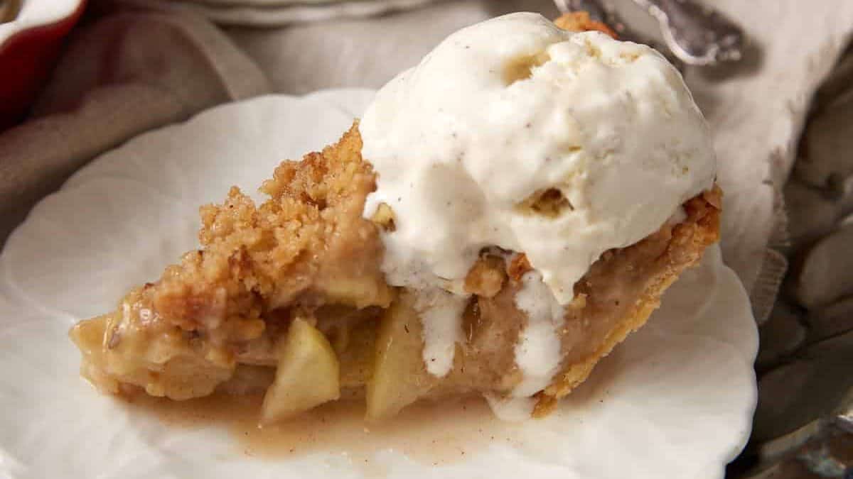 A slice of apple pie with ice cream dripping down the side.