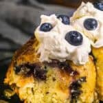 Close-up of a slice of peach blueberry cake topped with whipped cream and fresh blueberries on a black plate.