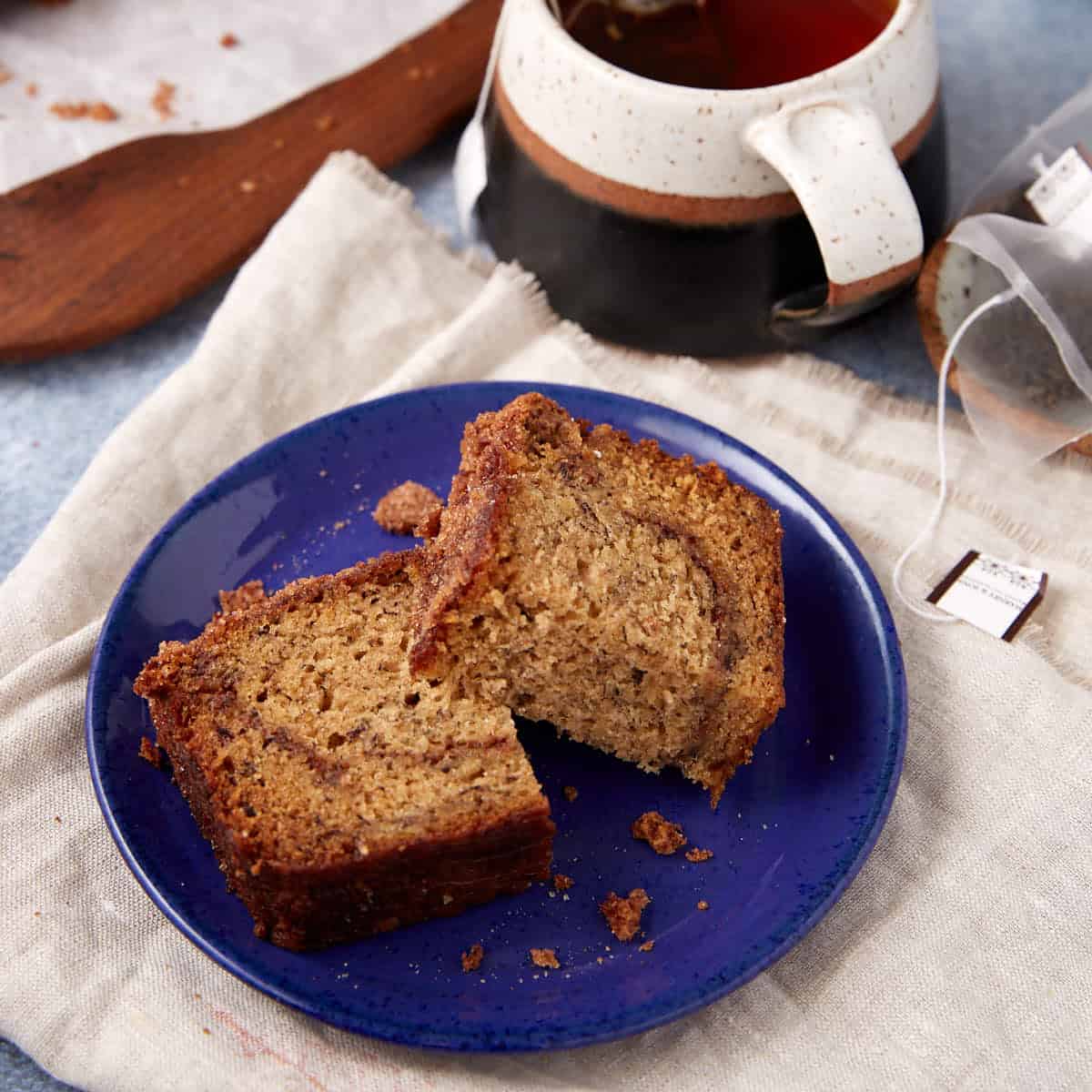 Two slices of snickerdoodle banana bread on a blue plate with a mug of tea in the background.