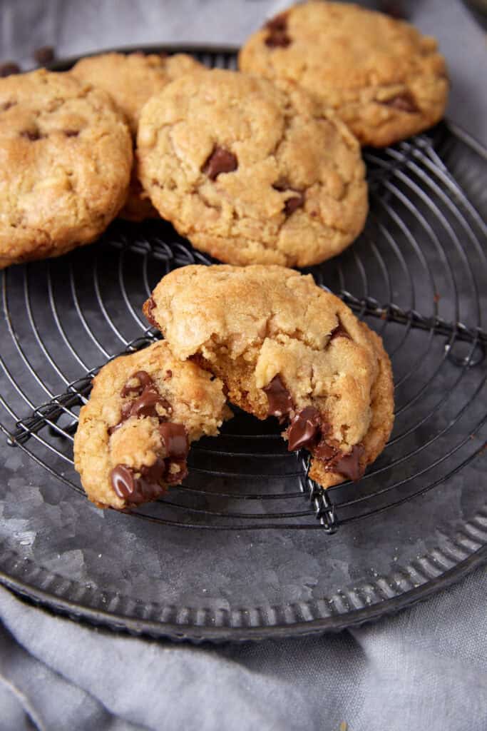 Toffee chocolate chip cookies on a round cooling rack, with one cookie broken open to show melted chocolate chips.