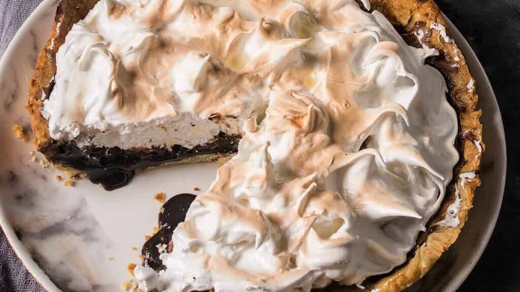 Partially sliced chocolate meringue pie on a plate, with a slice served on a white plate in the background.
