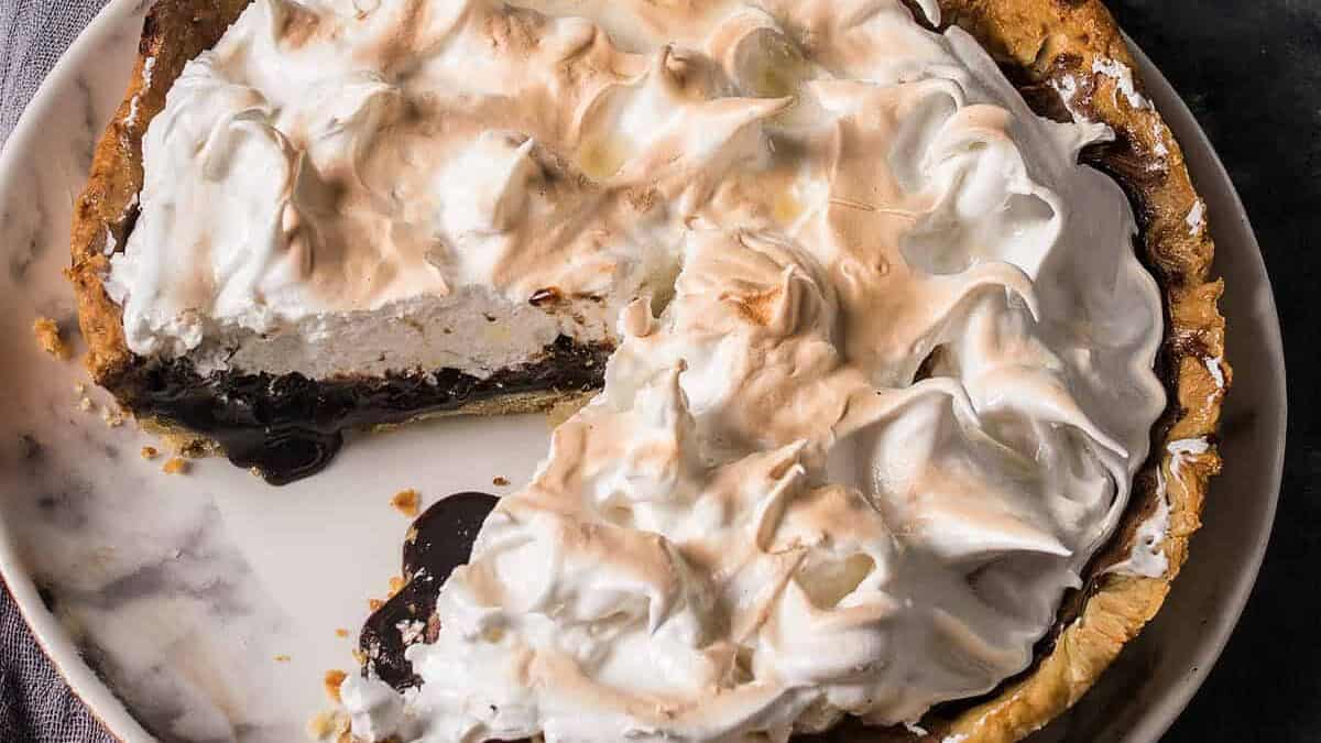 Partially sliced chocolate meringue pie on a plate, with a slice served on a white plate in the background.