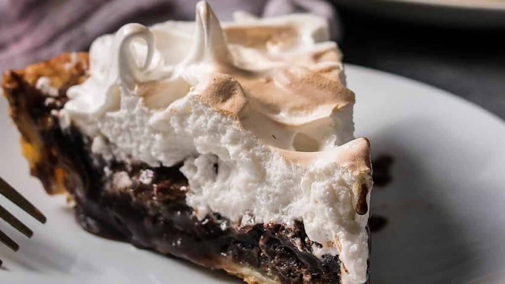 Close-up slice of chocolate meringue pie on a plate, focusing on the layers of filling and topping.