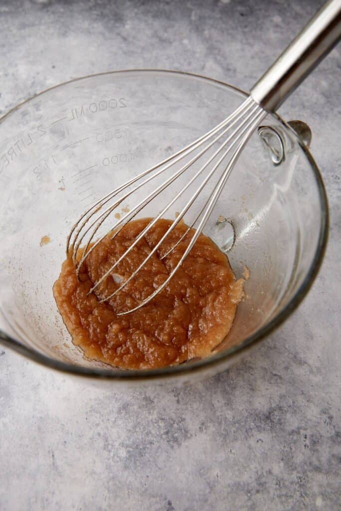 Melted butter and sugar mixture sits in a glass bowl with a whisk.