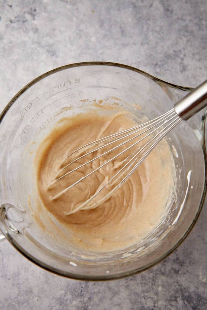 Whisked buttermilk pie filling looks smooth and lightly foamy in a glass mixing bowl.