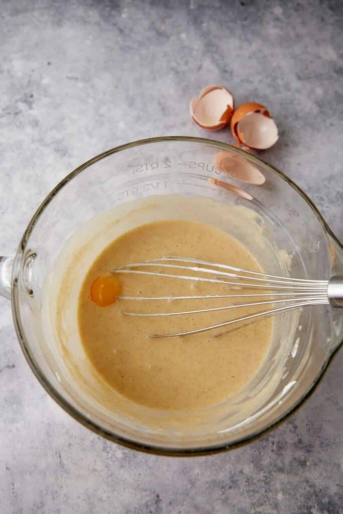 Egg yolk sits in a bowl of buttermilk pie filling with a whisk resting inside.