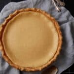 Baked buttermilk pie in a glass pie plate on a gray cloth with a pie server and forks nearby.