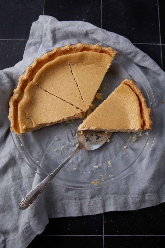 Baked buttermilk pie with several slices cut and one slice lifted out on a clear pie plate.