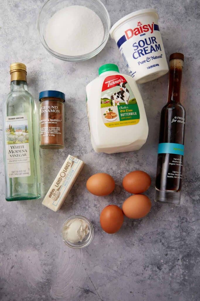 Buttermilk pie ingredients are arranged on a counter, including buttermilk, sour cream, eggs, vanilla, and cinnamon.