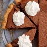 Close-up of a sliced chocolate chess pie in a glass pie plate topped with whipped cream.