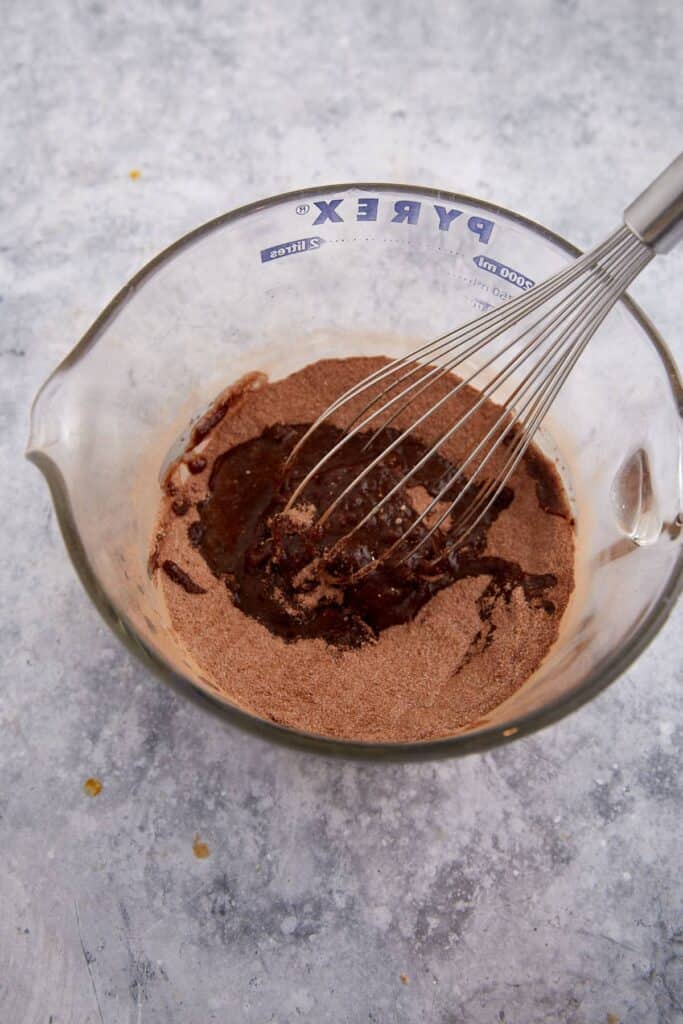 Melted butter is poured into the cocoa and sugar mixture in a glass bowl before whisking.