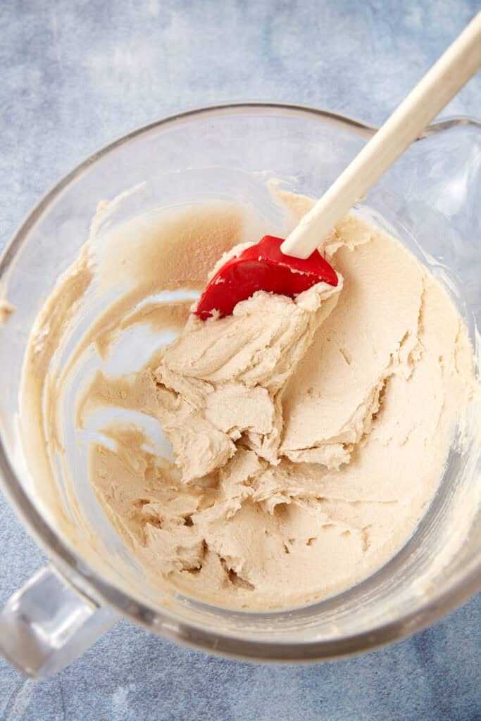 Mixing bowl of smooth blondie batter after creaming, with a red spatula resting on top.