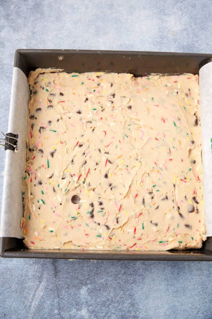 Sprinkle blondie dough pressed evenly into a parchment-lined baking pan before baking.