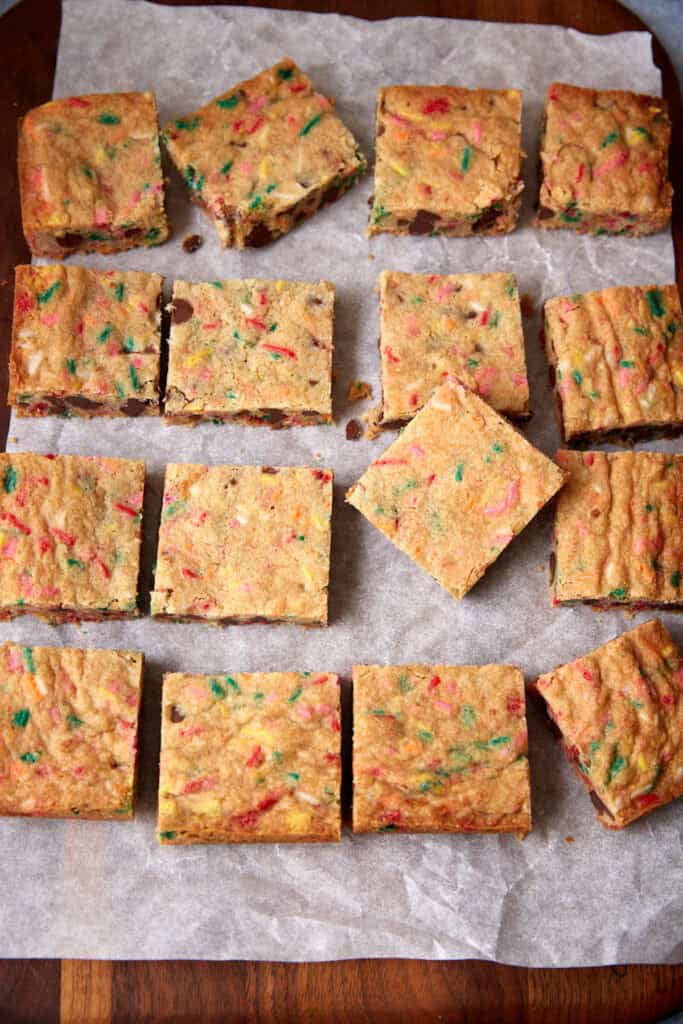Square-cut sprinkle blondies arranged on parchment paper, showing colorful sprinkles and chocolate chips in each piece.