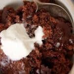 Close-up of a serving of slow cooker chocolate lava cake in a beige bowl, showing the gooey chocolate center topped with melting vanilla ice cream and a spoon tucked into the side.